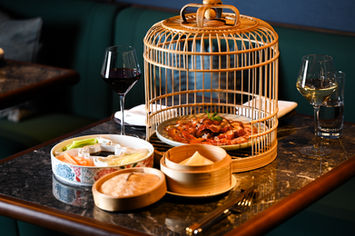 Dinner table with birdcage dim sum, red wine, and various Asian dishes.