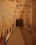 Narrow corridor with colorful ancient mural art to dark doorways.