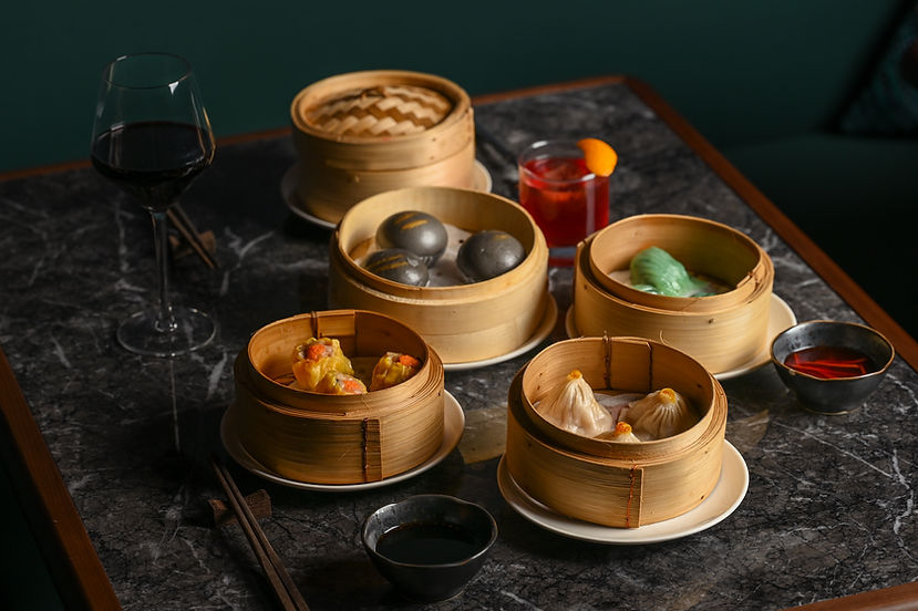 Assortment of dim sum in bamboo steamers with wine and cocktail.